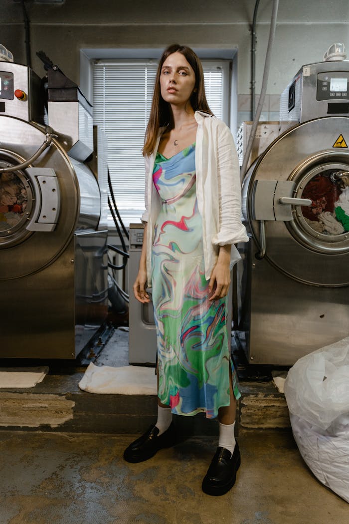 Stylish woman in a colorful dress standing between industrial washing machines.